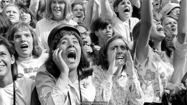 Screaming Beatles fans cheer for their idols on the streets of New York City, USA as the British pop group arrive for their Amer